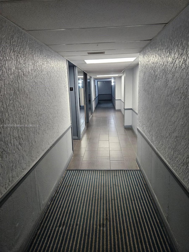 corridor with a drop ceiling and tile patterned flooring