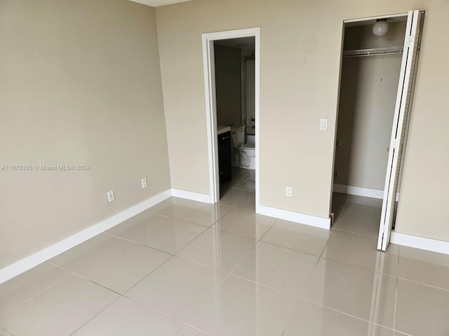 unfurnished bedroom with a closet, ensuite bath, and light tile patterned floors