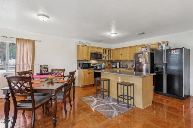 kitchen featuring a kitchen breakfast bar, black appliances, a center island, tile patterned floors, and backsplash