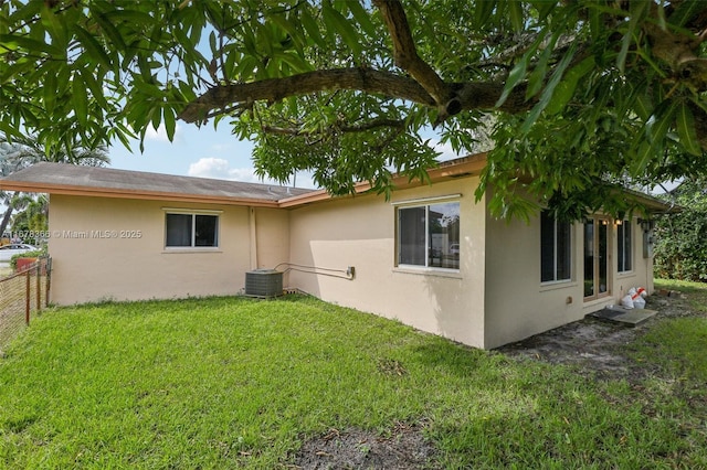 rear view of property with central air condition unit and a lawn