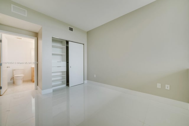 unfurnished bedroom featuring connected bathroom, tile patterned floors, and a closet