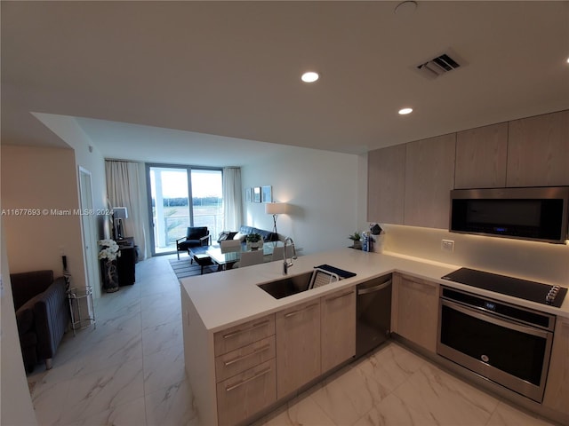 kitchen with appliances with stainless steel finishes, kitchen peninsula, sink, and light brown cabinetry