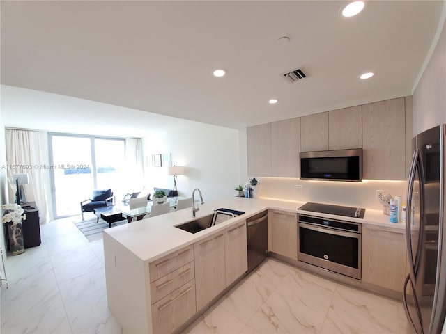 kitchen with stainless steel appliances, light brown cabinetry, sink, and kitchen peninsula