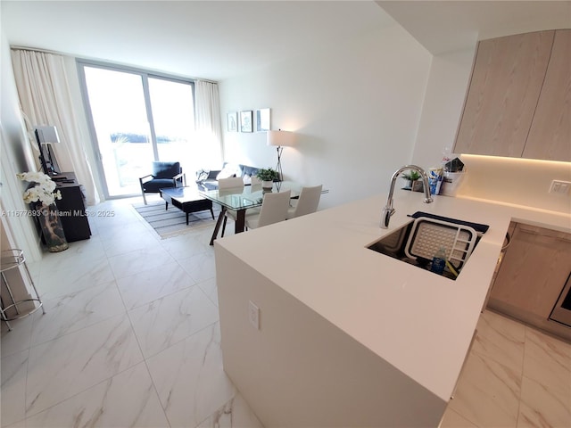 kitchen with a peninsula, marble finish floor, a wall of windows, light countertops, and a sink