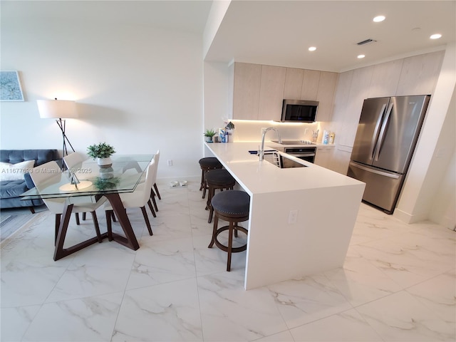 kitchen with recessed lighting, a sink, appliances with stainless steel finishes, modern cabinets, and a kitchen bar