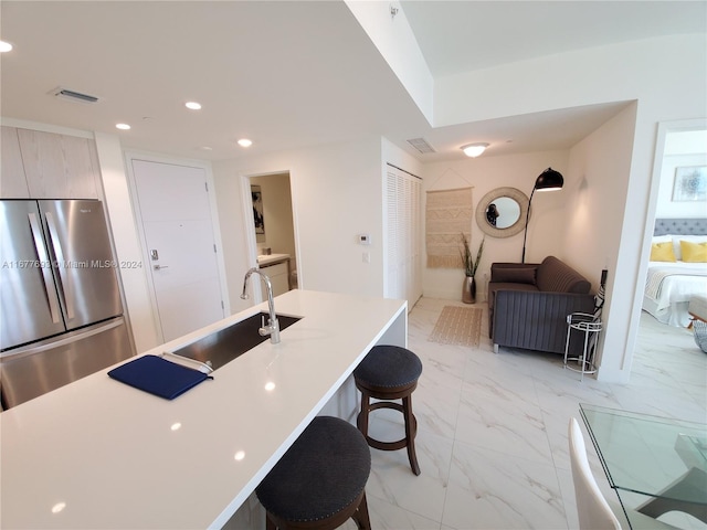 kitchen featuring sink, stainless steel fridge, an island with sink, and a kitchen breakfast bar