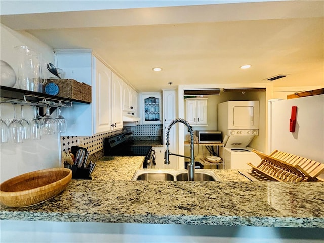 kitchen with sink, white cabinets, range hood, stacked washing maching and dryer, and decorative backsplash