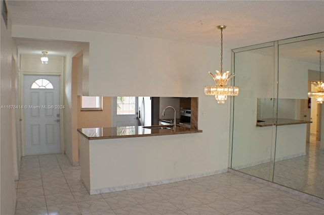 kitchen with kitchen peninsula, stainless steel fridge, a textured ceiling, sink, and decorative light fixtures