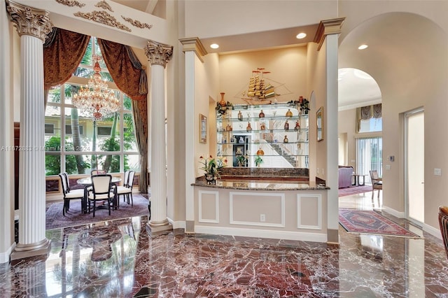 bar with decorative columns, stone counters, a towering ceiling, and a chandelier