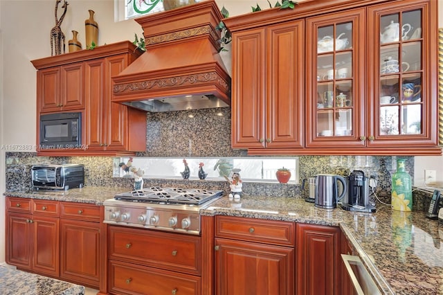 kitchen featuring light stone countertops, tasteful backsplash, custom range hood, black microwave, and stainless steel gas cooktop