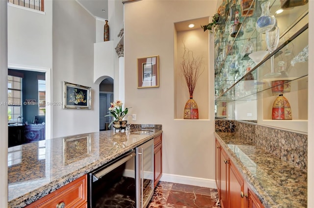 bar featuring wine cooler, light stone counters, sink, and a high ceiling