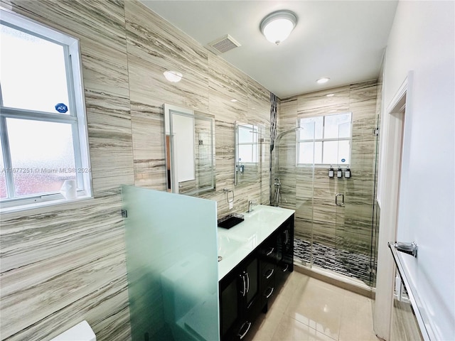 bathroom featuring tile patterned flooring, vanity, a shower with shower door, and tile walls