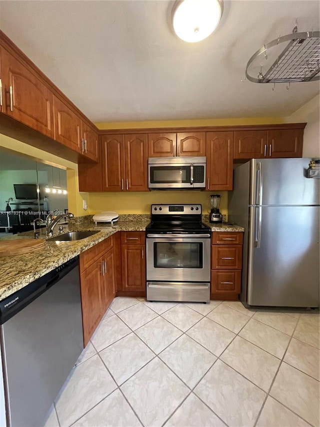 kitchen featuring light stone countertops, brown cabinets, a sink, light tile patterned floors, and stainless steel appliances