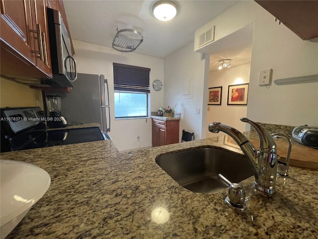 kitchen featuring black / electric stove, visible vents, a sink, stainless steel microwave, and stone counters