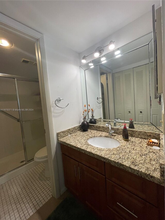 bathroom featuring vanity, toilet, tile patterned floors, and a shower with shower door