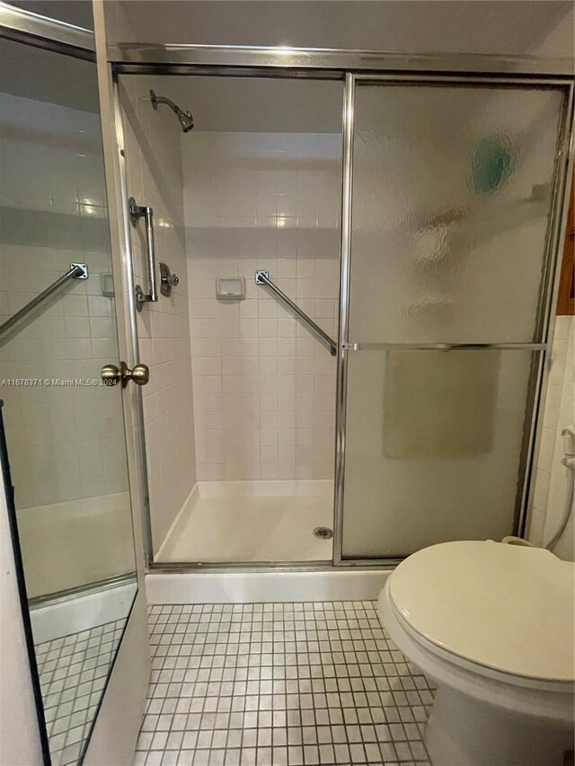 bathroom featuring toilet, tile patterned flooring, and a stall shower