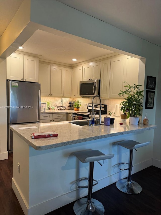 kitchen featuring kitchen peninsula, backsplash, white cabinetry, dark wood-type flooring, and stainless steel appliances