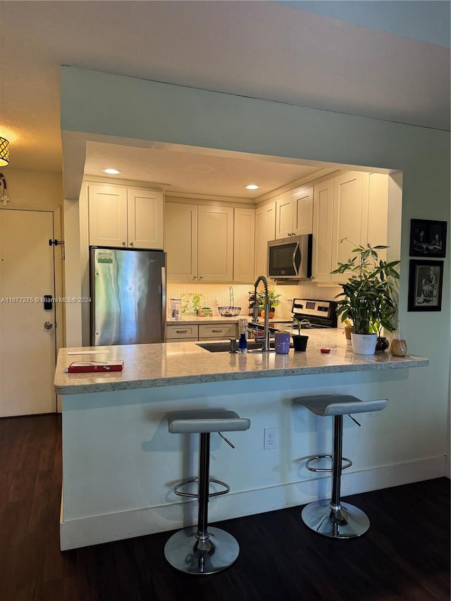 kitchen featuring kitchen peninsula, a kitchen breakfast bar, white cabinetry, stainless steel appliances, and dark wood-type flooring