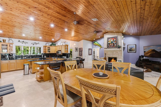 dining space featuring vaulted ceiling, a stone fireplace, and wood ceiling