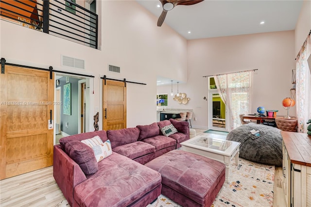 living room featuring ceiling fan, a barn door, light hardwood / wood-style flooring, and a high ceiling