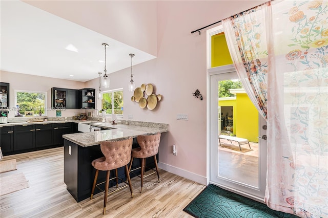 kitchen with kitchen peninsula, sink, a kitchen breakfast bar, light hardwood / wood-style floors, and light stone counters