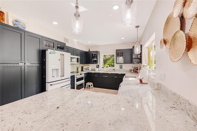 kitchen with high end white refrigerator, sink, range with two ovens, hanging light fixtures, and light stone countertops