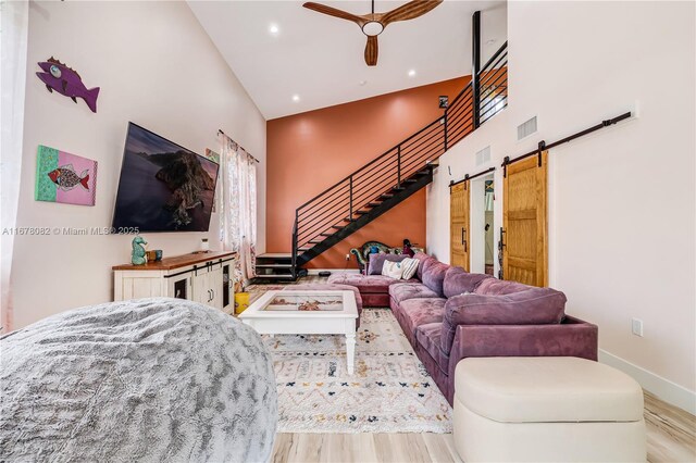 living room with light hardwood / wood-style flooring, a barn door, ceiling fan, and a high ceiling