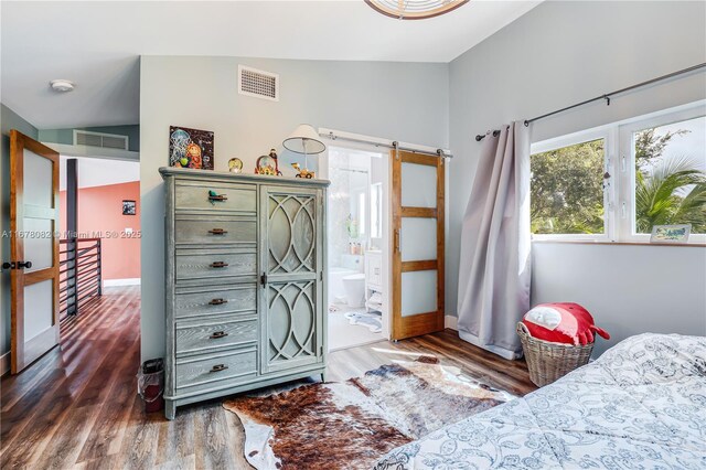 bedroom with dark hardwood / wood-style flooring, a barn door, and ensuite bathroom