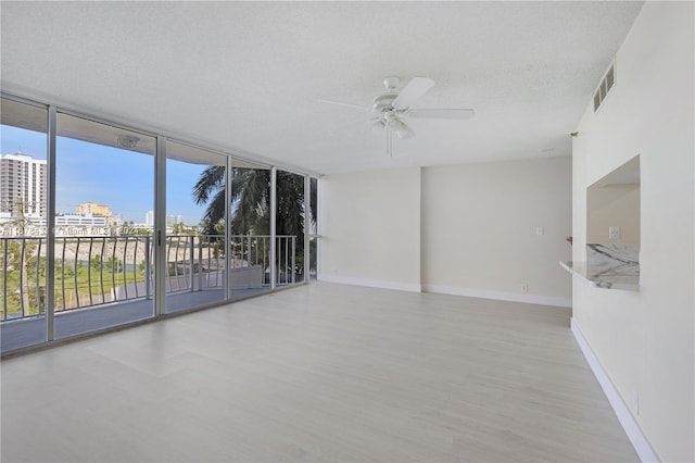 spare room with a wall of windows, a textured ceiling, light wood-type flooring, and ceiling fan