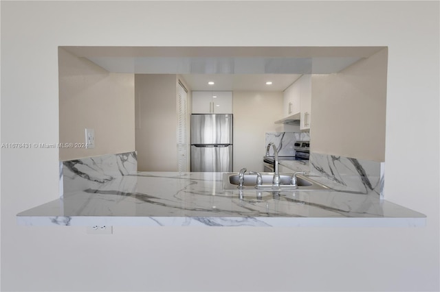 kitchen with decorative backsplash, stainless steel appliances, sink, light stone countertops, and white cabinetry