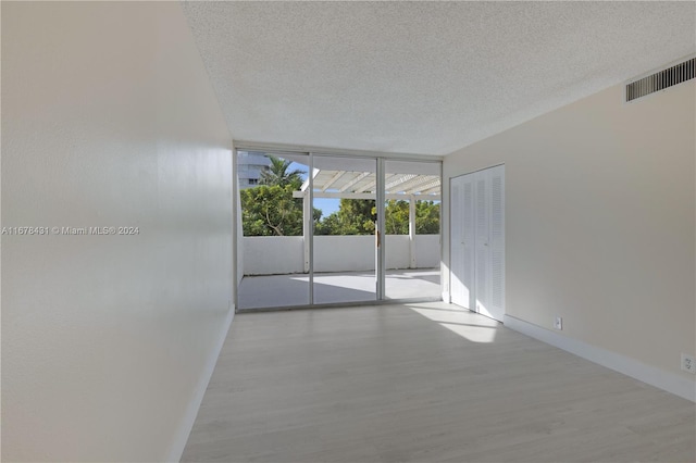 spare room with expansive windows, a textured ceiling, and light hardwood / wood-style floors