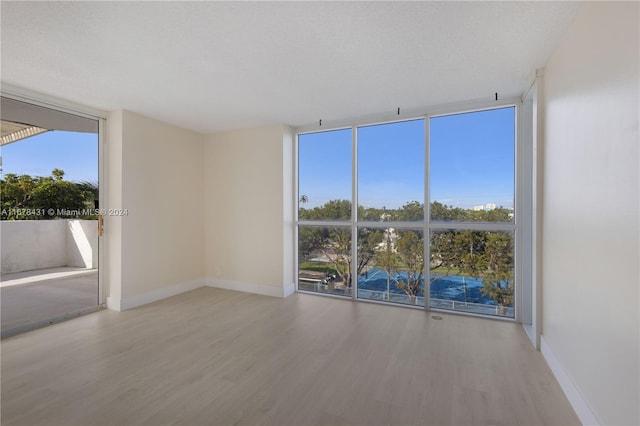 unfurnished room with a wall of windows, light hardwood / wood-style flooring, and a textured ceiling