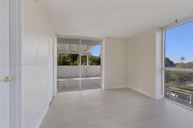 unfurnished room with a wall of windows, a textured ceiling, and light hardwood / wood-style floors