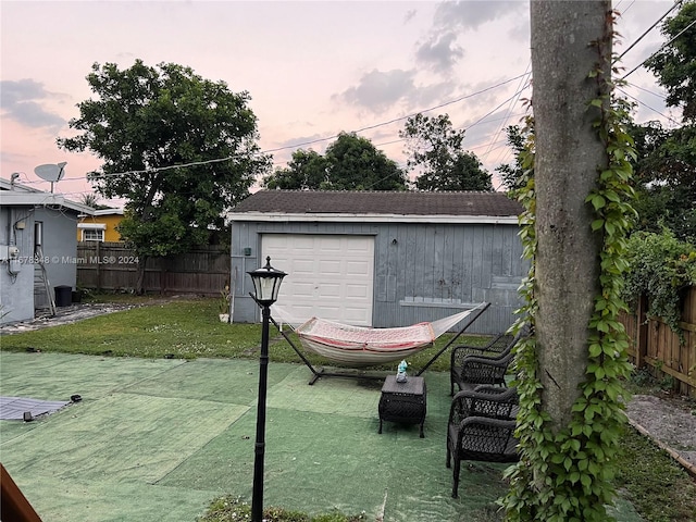 patio terrace at dusk with a yard, an outdoor structure, and a garage