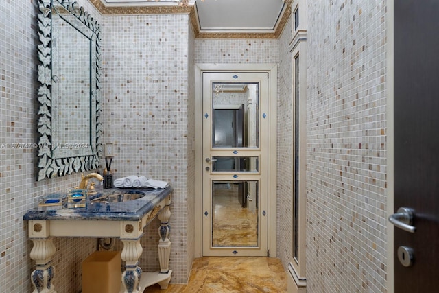 bathroom with crown molding, sink, and tile walls