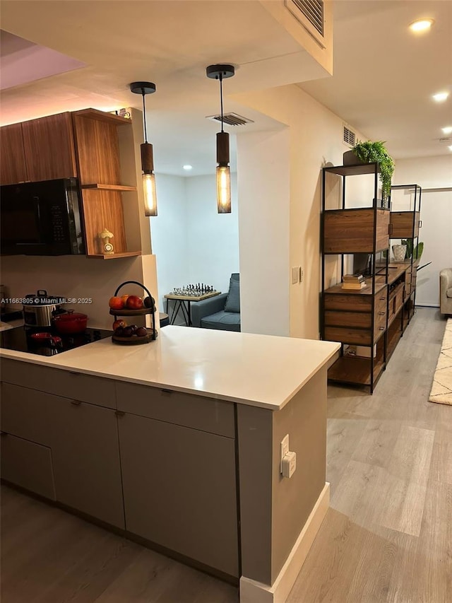 kitchen featuring kitchen peninsula, stovetop, decorative light fixtures, and light hardwood / wood-style flooring