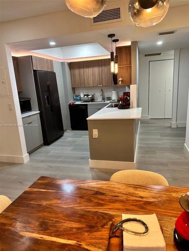 kitchen with pendant lighting, black appliances, sink, light hardwood / wood-style floors, and kitchen peninsula