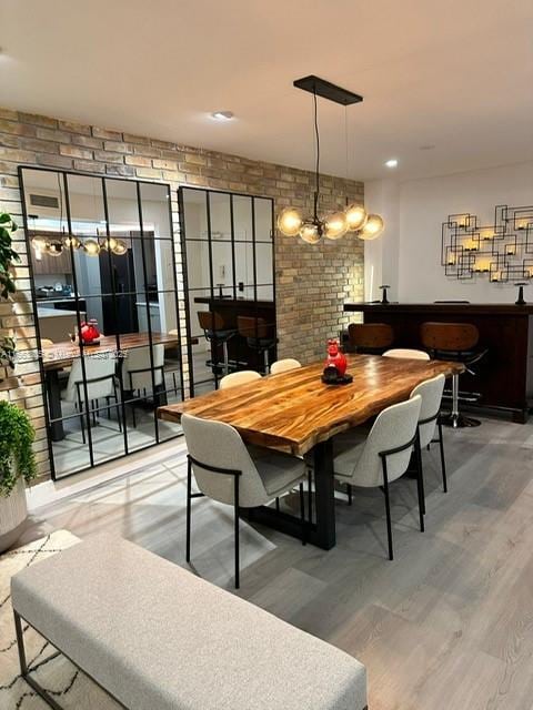 dining area featuring hardwood / wood-style floors, a notable chandelier, and brick wall