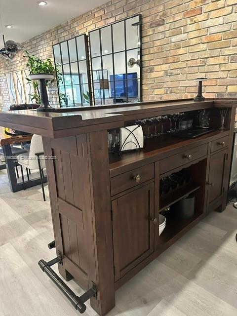 bar featuring dark brown cabinetry and brick wall