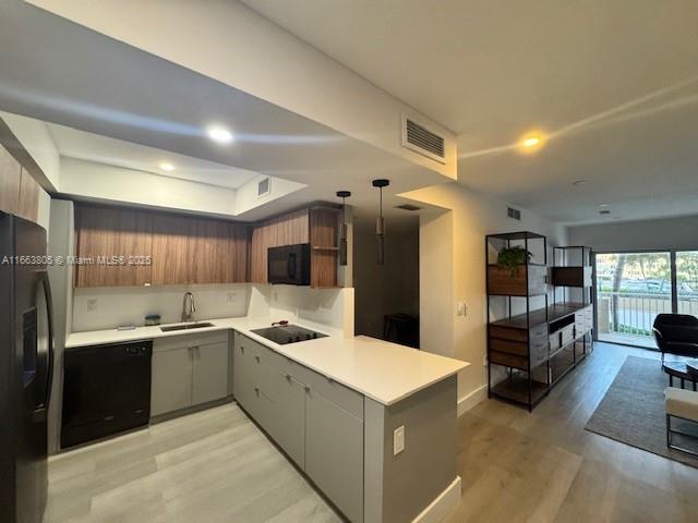 kitchen with sink, hanging light fixtures, kitchen peninsula, light hardwood / wood-style floors, and black appliances