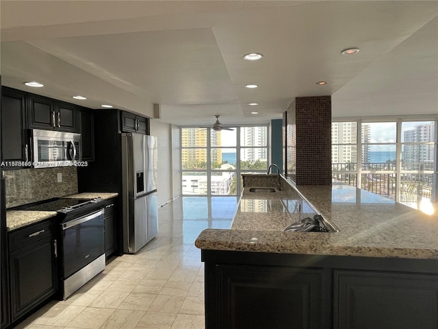 kitchen featuring sink, decorative backsplash, ceiling fan, appliances with stainless steel finishes, and light stone counters