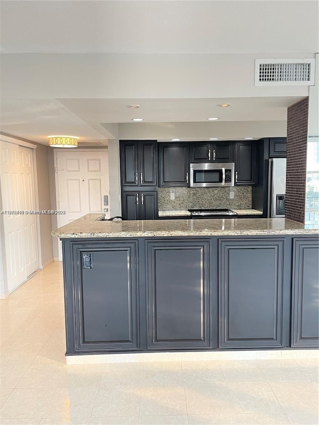 kitchen with light stone countertops, backsplash, kitchen peninsula, light tile patterned flooring, and appliances with stainless steel finishes