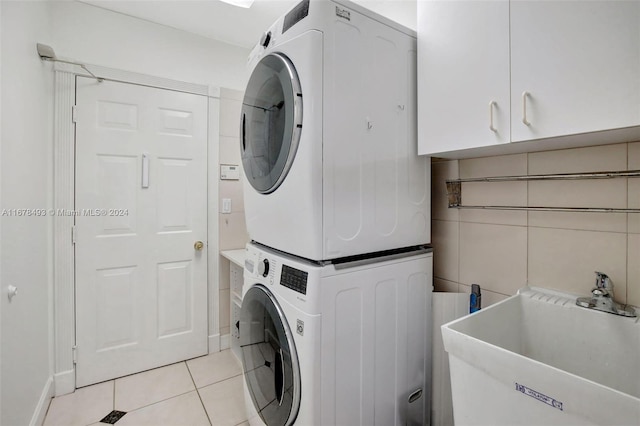 washroom with light tile patterned flooring, cabinets, sink, and stacked washer and clothes dryer