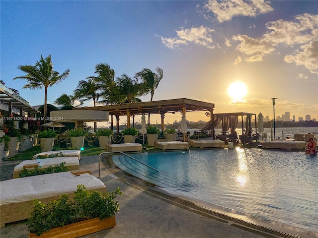 pool at dusk with a water view and a pergola