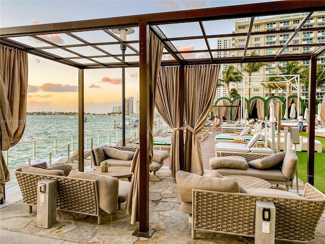 patio terrace at dusk featuring outdoor lounge area, a water view, and a pergola