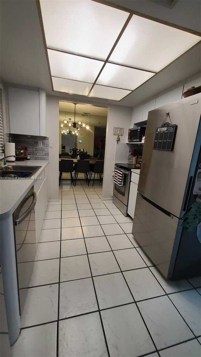 kitchen with appliances with stainless steel finishes, a notable chandelier, white cabinetry, and light tile patterned floors