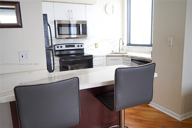 kitchen featuring white cabinets, stainless steel appliances, light wood-type flooring, and tasteful backsplash