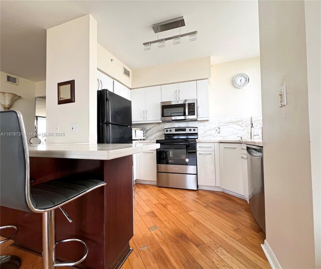 kitchen with appliances with stainless steel finishes, white cabinets, sink, and light wood-type flooring