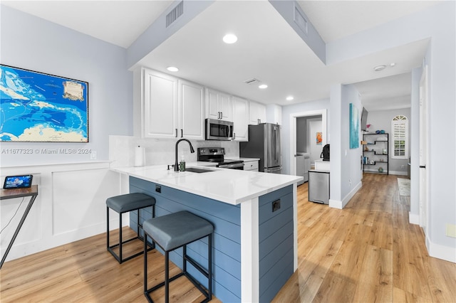 kitchen featuring white cabinets, appliances with stainless steel finishes, a kitchen bar, light wood-type flooring, and sink