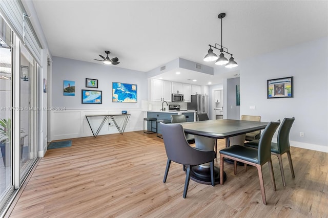 dining space with sink, light wood-type flooring, and ceiling fan